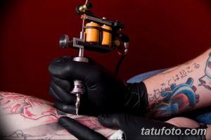 Фото процесса нанесения татуировки на руку. Мастер в черных перчатках работает над рисунком с японскими мотивами.